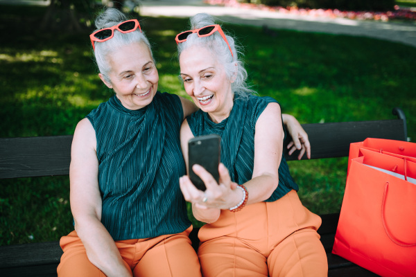 Senior women twins outdoors in city checking a smartphone.