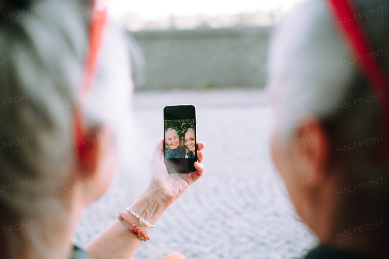 Senior women twins outdoors in a city park taking and chcecking selfie.