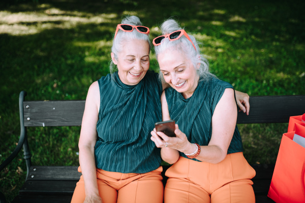 Senior women twins outdoors in city checking a smartphone.