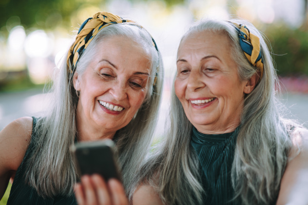 Senior women twins outdoors in city checking a smartphone.