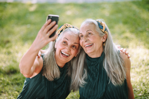 Senior women twins outdoors in a city park taking selfie.