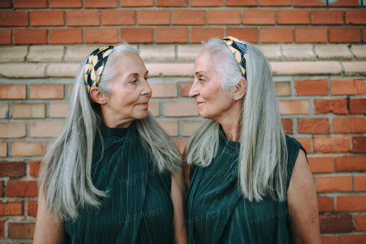 Portrait of senior women, twins,in same clothes standing back to back, outdoor in a city.