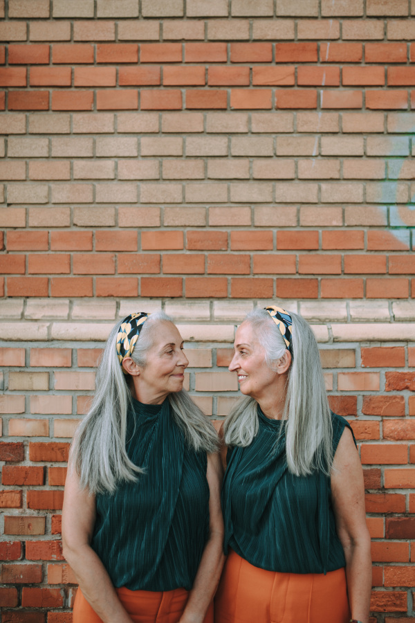 Portrait of senior women, twins,in same clothes standing back to back, outdoor in a city.