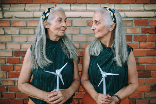 Senior women, twins holding a plastic model of wind turbine, concept of future, ecology and renewable resources, message for next generation.