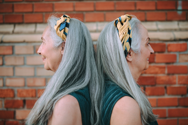 Side view of senior women, twins,in same clothes standing back to back, outdoor in a city.