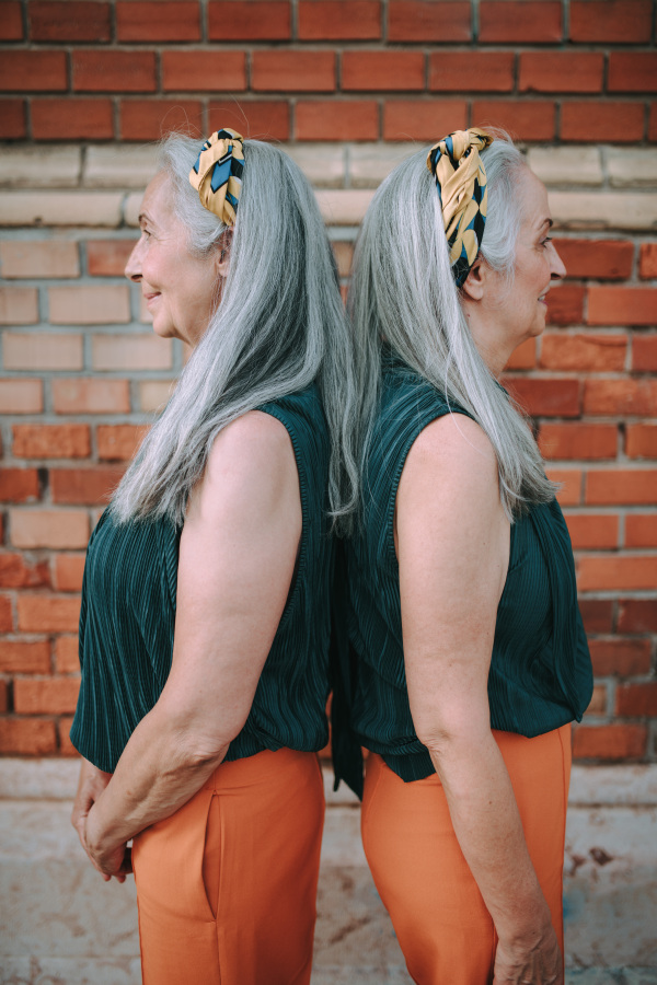 Side view of senior women, twins,in same clothes standing back to back, outdoor in a city.