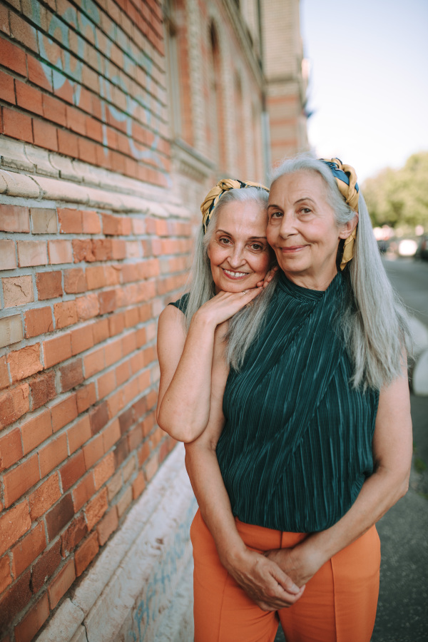 Senior women twins,in same clothes standing and posing in front of a brick wall, outdoor in city.