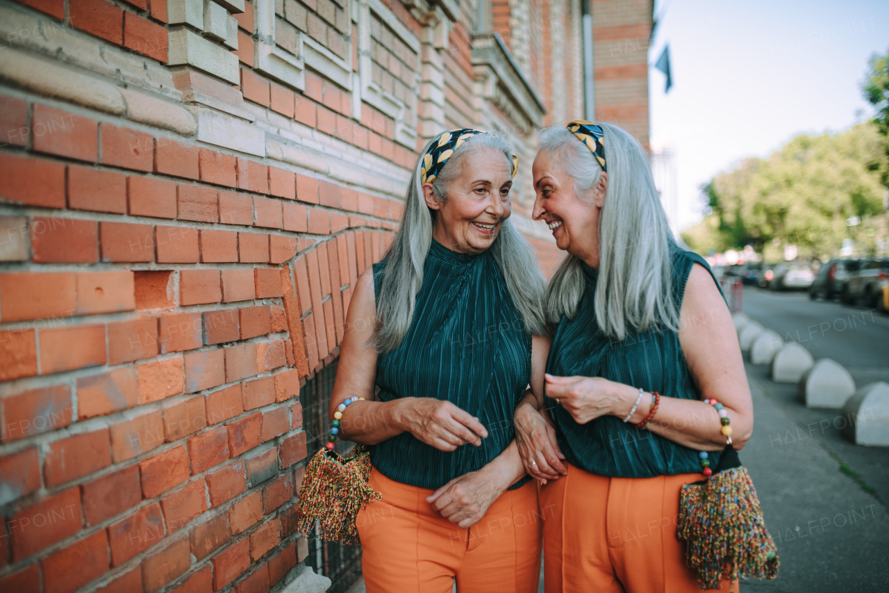 Happy senior twins in same clothes talking and walking in a city.