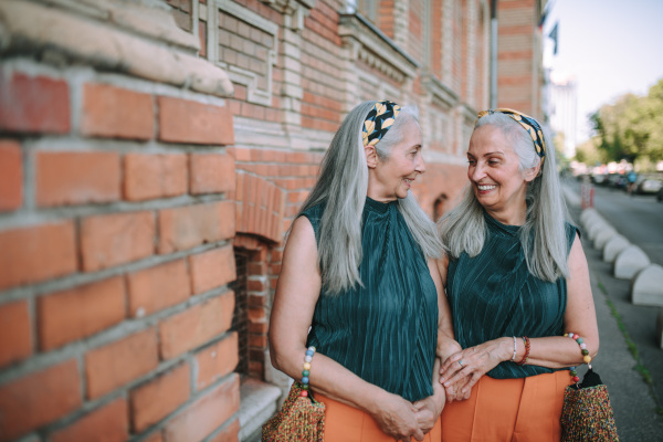 Happy senior twins in same clothes talking and walking in a city.