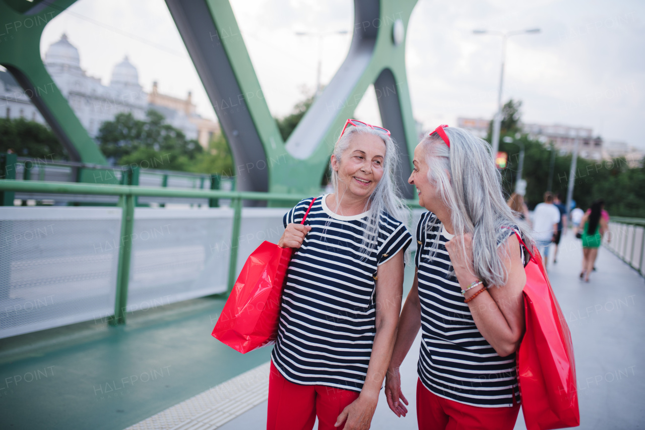 Happy senior twins in same clothes walking in a city, returning from shopping.