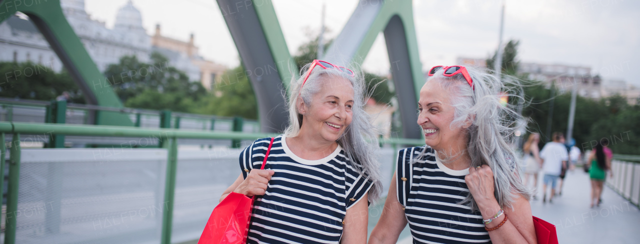 Happy senior twins in same clothes walking in a city, returning from shopping.