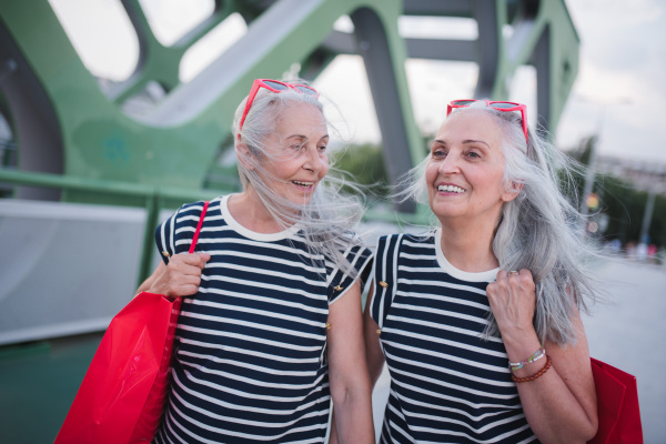 Happy senior twins in same clothes walking in a city, returning from shopping.