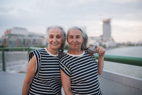 Portrait of happy seniors women, twins in the same clothes, walking on city bridge.