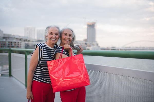 Happy senior twins in same clothes walking in a city, returning from shopping.