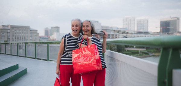 Happy senior twins in same clothes walking in a city, returning from shopping.