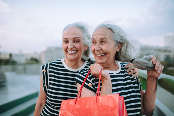 Happy senior twins in same clothes walking in a city, returning from shopping.