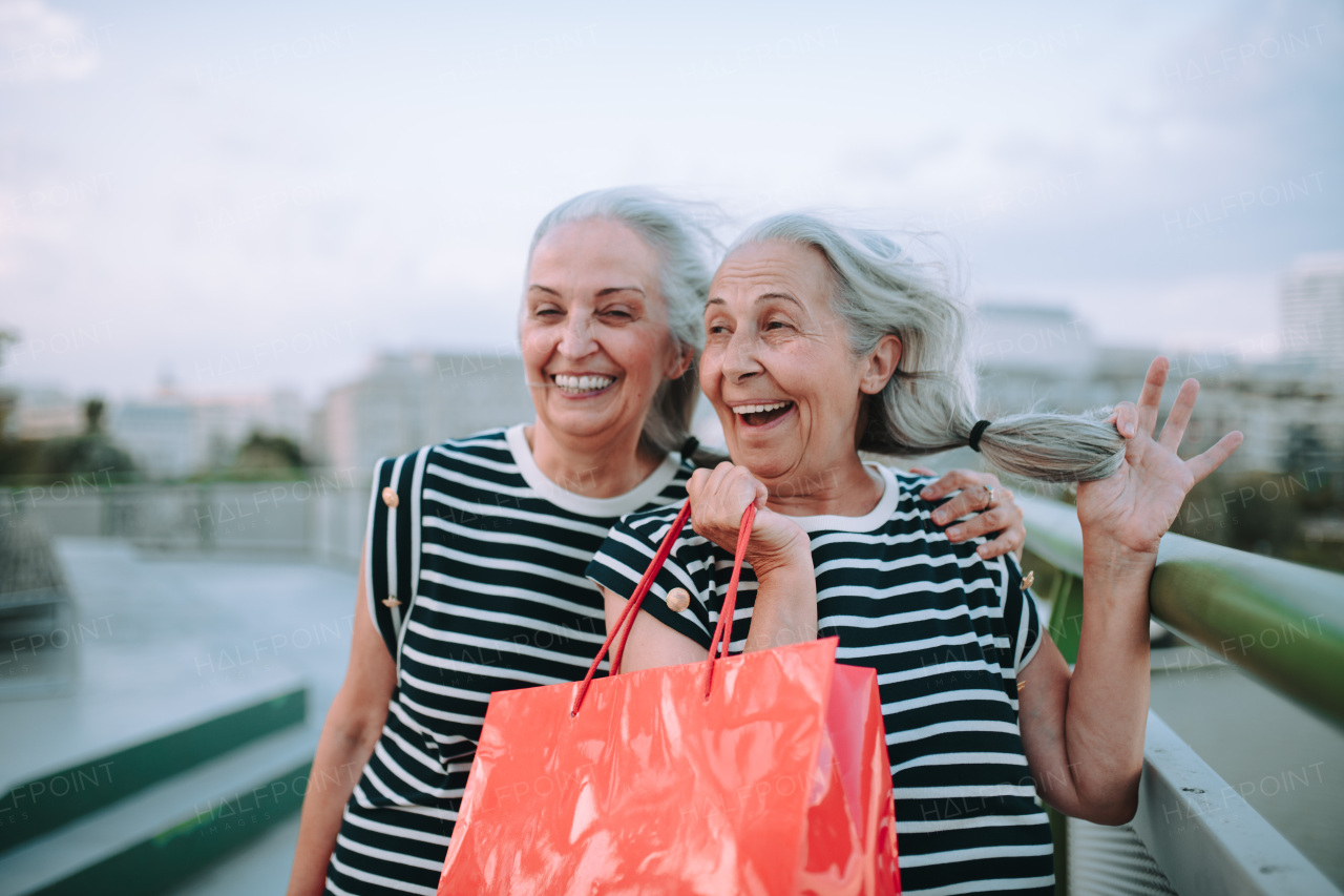 Happy senior twins in same clothes walking in a city, returning from shopping.