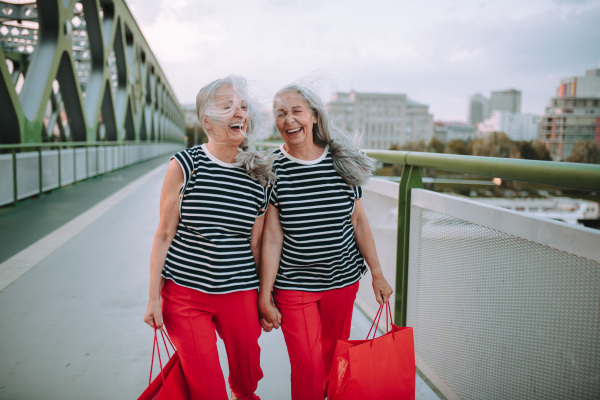 Happy senior twins in same clothes walking in a city, returning from shopping.