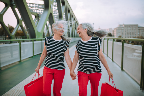 Happy senior twins in same clothes walking in a city, returning from shopping.