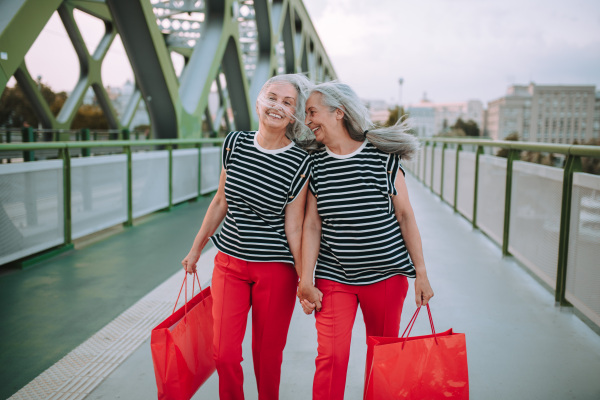 Happy senior twins in same clothes walking in a city, returning from shopping.