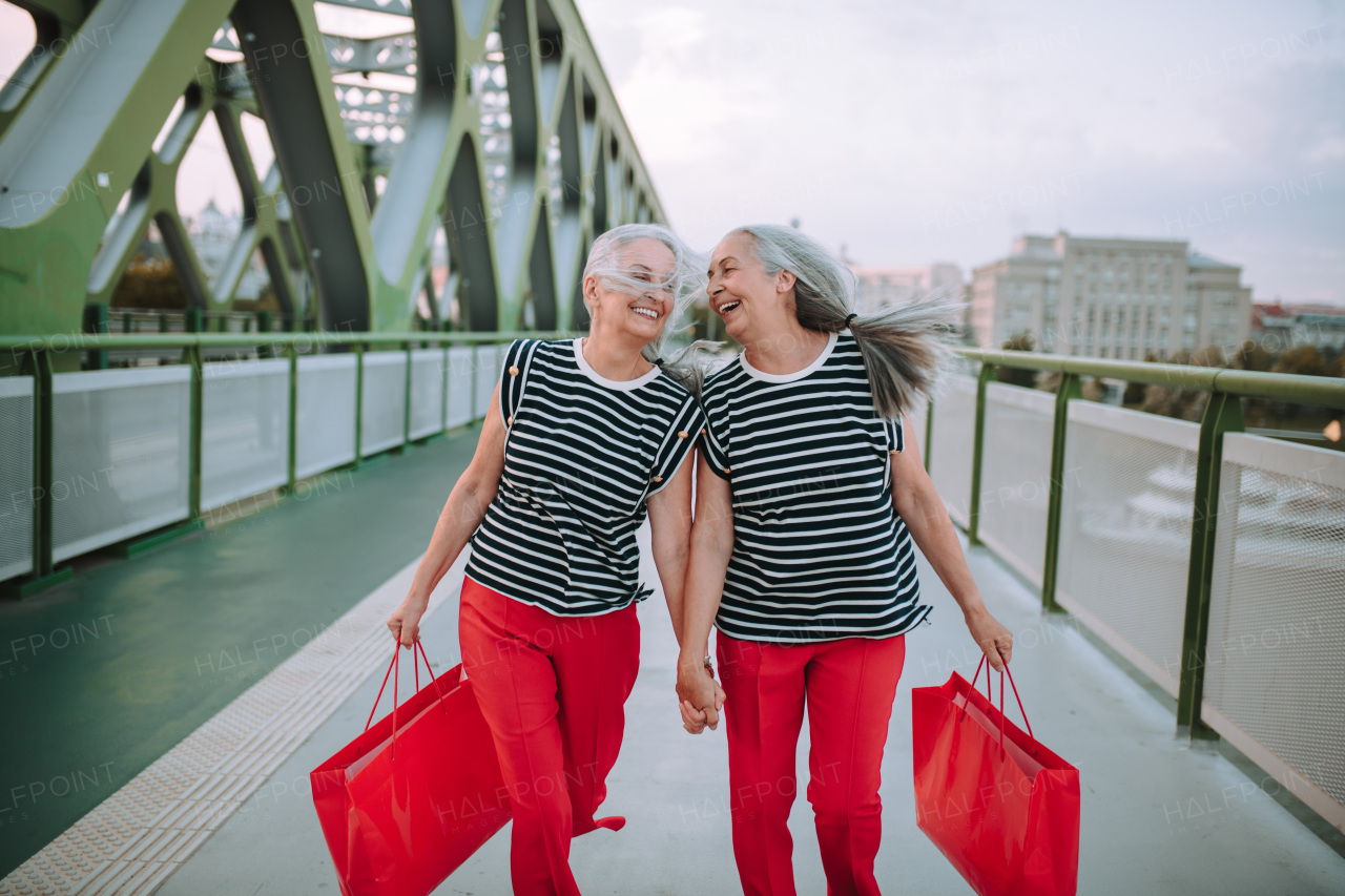 Happy senior twins in same clothes walking in a city, returning from shopping.