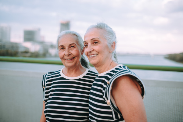 Portrait of happy seniors women, twins in the same clothes, walking on city bridge.