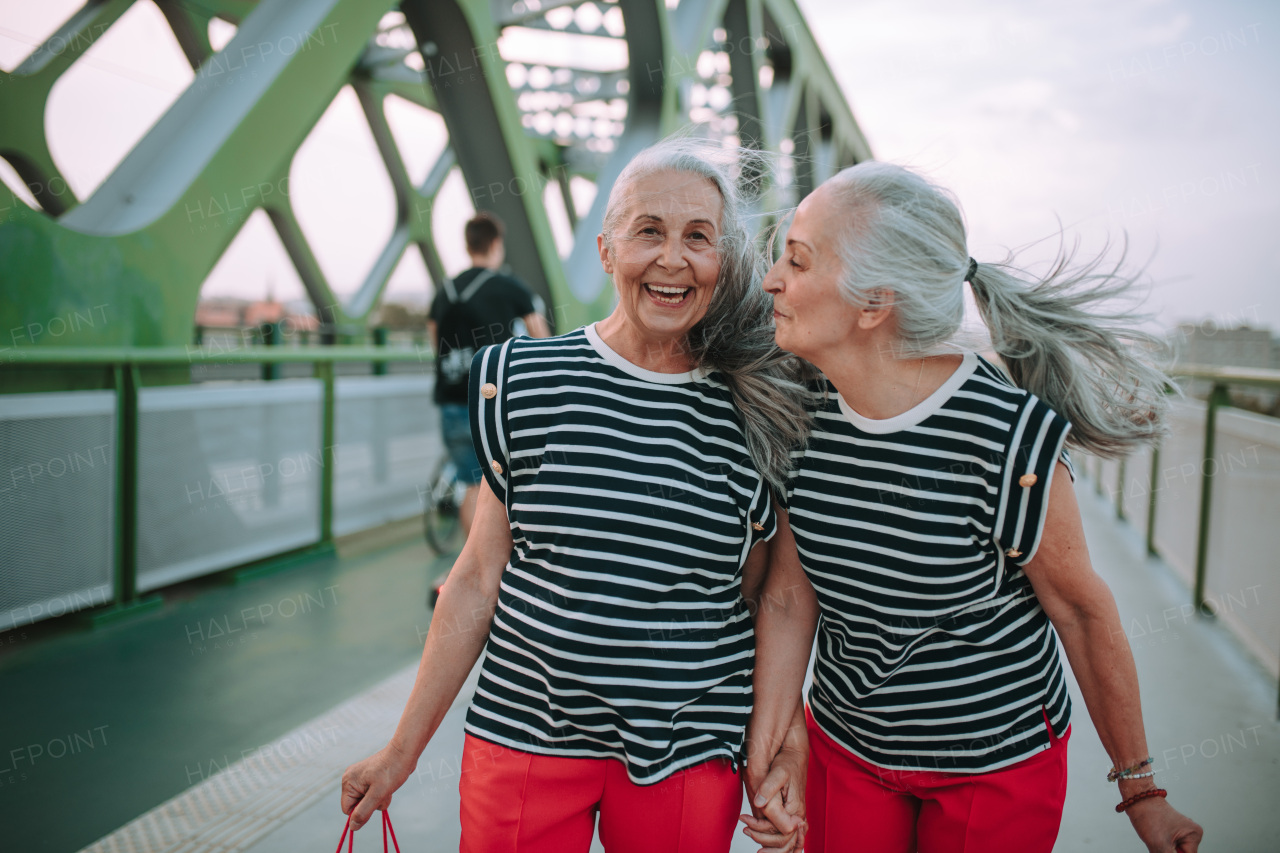 Happy senior twins in same clothes walking in a city, returning from shopping.