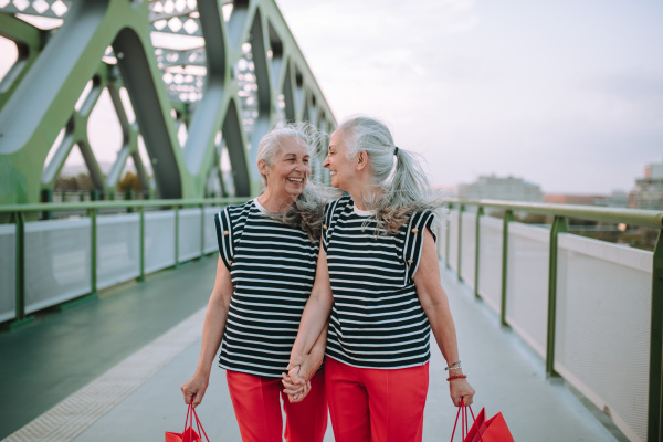 Happy senior twins in same clothes walking in a city, returning from shopping.