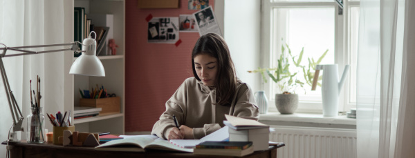 Young teenage girl studying and doing homework in her room.