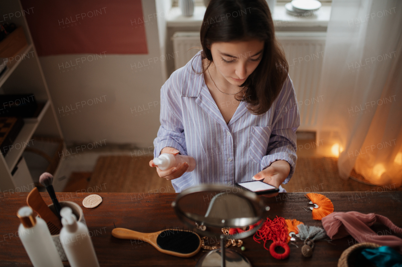 Teenage girl doing her skin care routine and checking her smartphone.