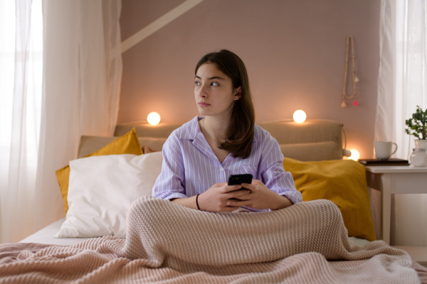 Young teenage girl srolling her smartphone in a room.