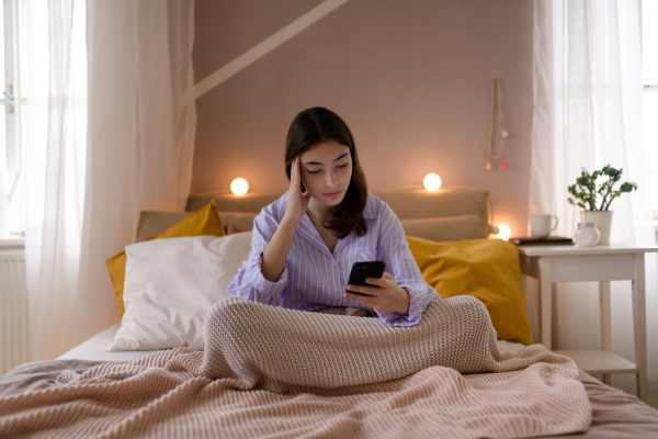 Young teenage girl srolling her smartphone in a room.