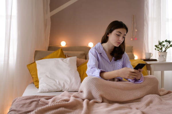 Young teenage girl srolling her smartphone in a room.