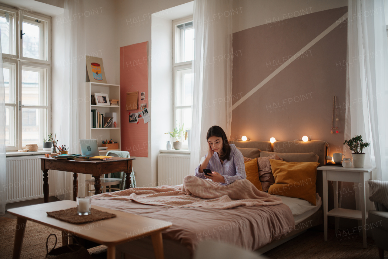 Young teenage girl srolling her smartphone in a room.