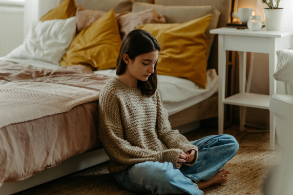 Unhappy teenage girl sitting on the floor in her room, koncept of mental health.