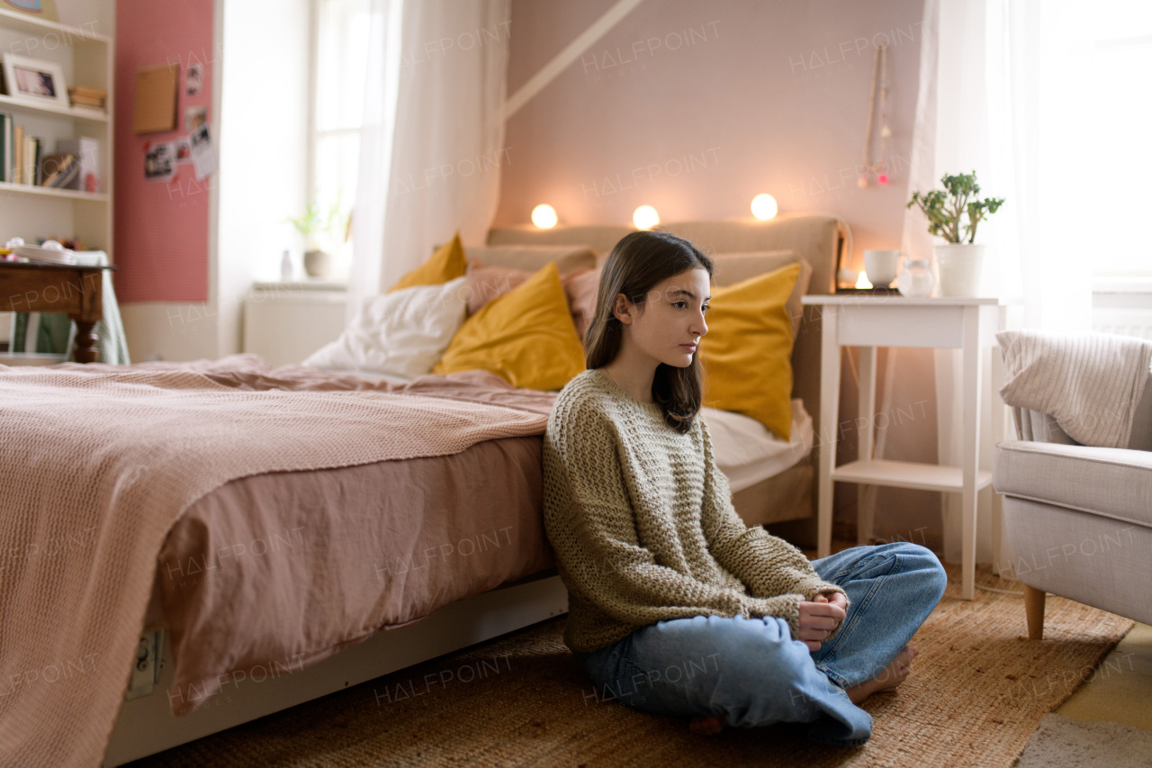 Unhappy teenage girl sitting on the floor in her room, koncept of mental health.