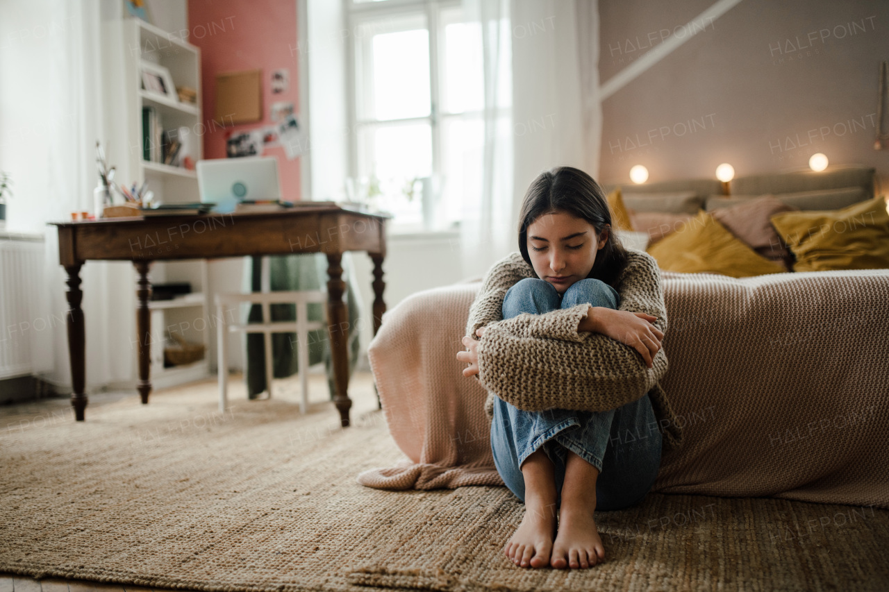 Teenage girl sitting on the floor with head on knees, koncept of mental health.