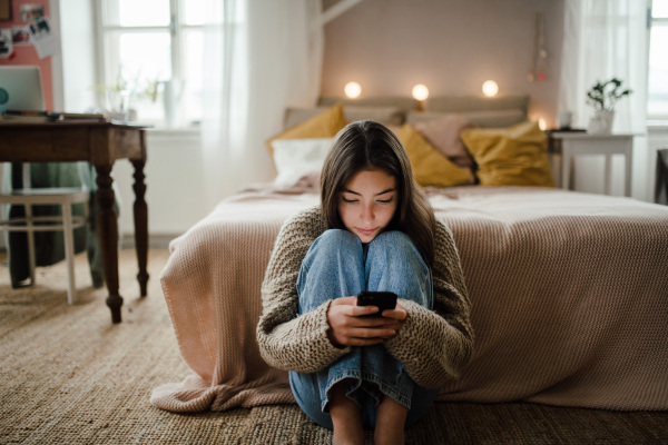 Teenage girl sitting on the floor and scrolling a smartphone.