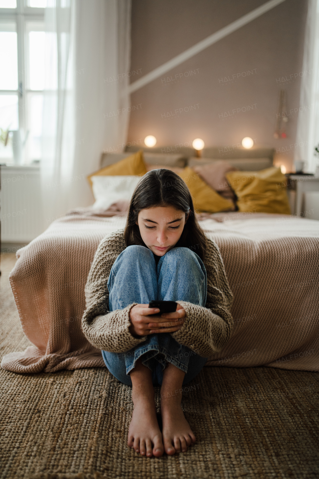 Teenage girl sitting on the floor and scrolling a smartphone.