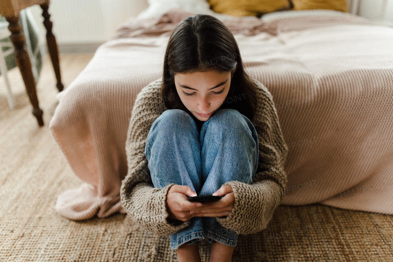 Teenage girl sitting on the floor and scrolling a smartphone.