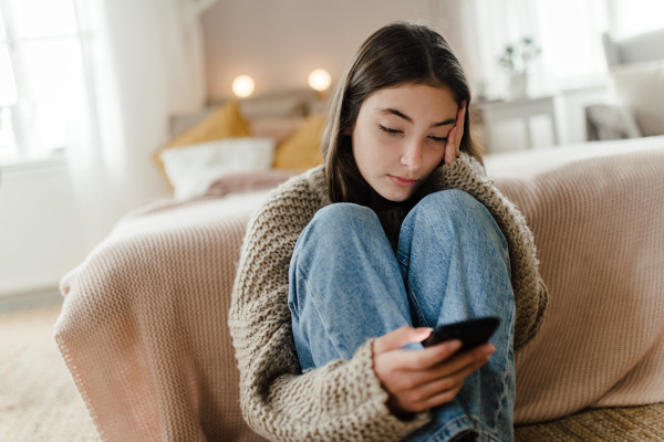 Teenage girl sitting on the floor and scrolling a smartphone.