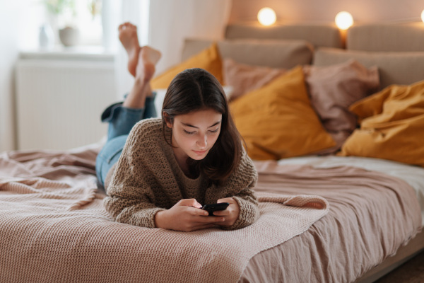 Young teenage girl srolling her smartphone in a room.