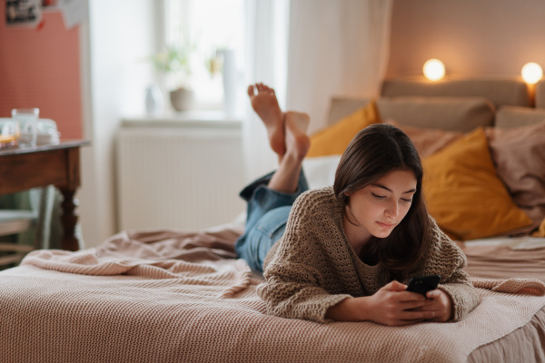 Young teenage girl srolling her smartphone in a room.