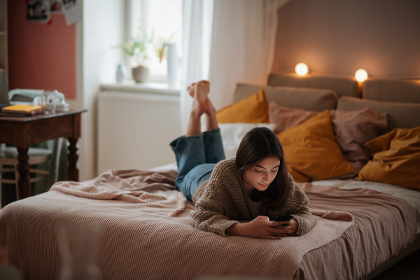 Young teenage girl srolling her smartphone in a room.