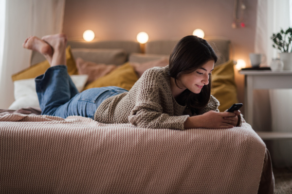 Young teenage girl srolling her smartphone in a room.