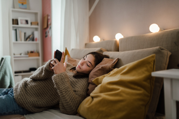 Young teenage girl srolling her smartphone in a room.