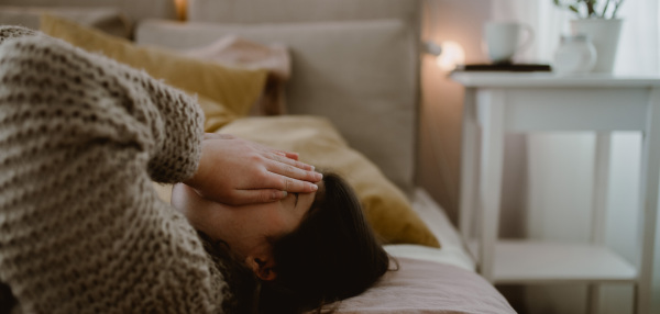 Unhappy girl lying in a bed with hands on her face.