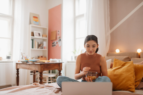 Young teenage girl looking moovie on her latop and eating something.