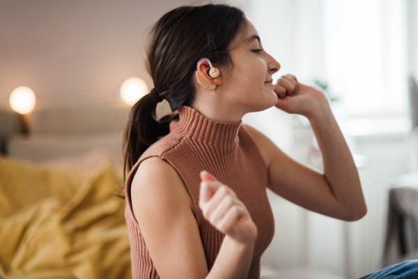 Teenage girl with hearing aid listening music in the room.