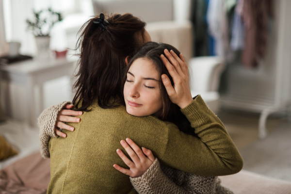 Young teenage girl hugging her mother at home.